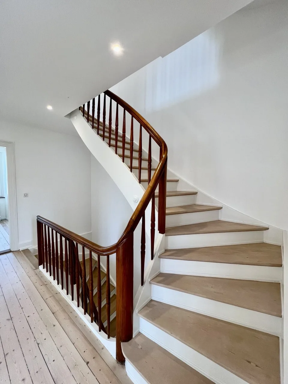 Escalier tournant avec marches claires, contremarches blanches, rampe foncée et parquet clair au sol