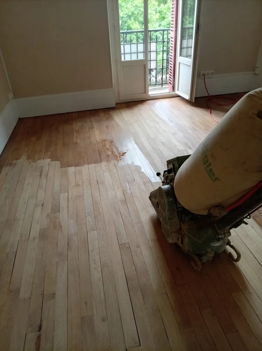 Ponçage à la ponceuse à bande d’un parquet massif lors d’une rénovation