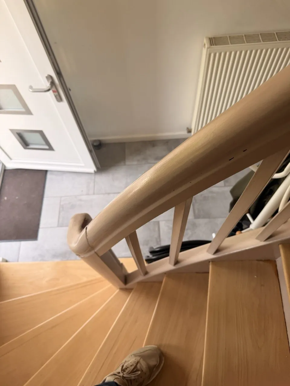 Ponçage de parquet à Wittenheim — Escalier d’entrée vu du haut : marches bois, main courante beige et carrelage gris dans le hall.