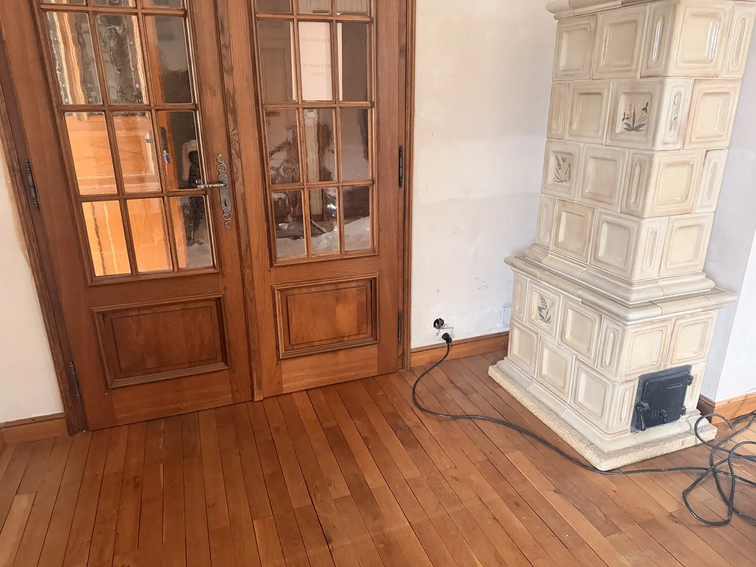 Parquet ciré avant rénovation autour d’un poêle en faïence impossible à déplacer