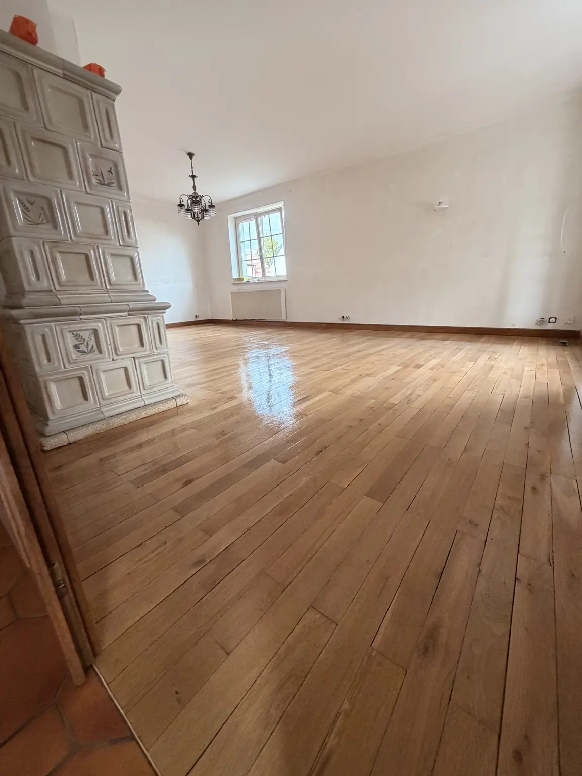 Parquet du salon rénové et vitrifié autour d’un poêle en faïence à Ottmarsheim