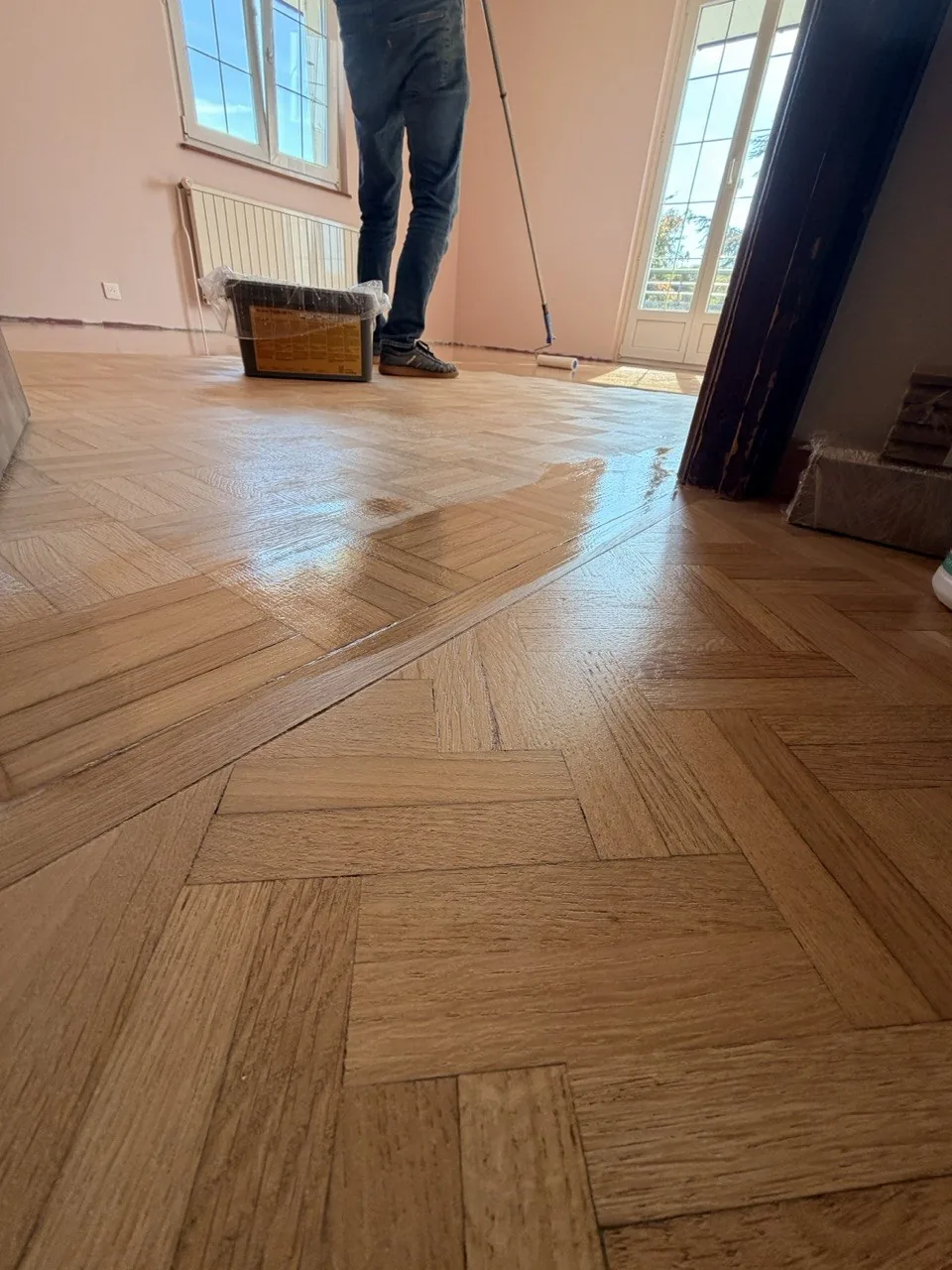 Application de la finition au rouleau sur perche sur un parquet mosaïque, bac de produit doublé d’un film