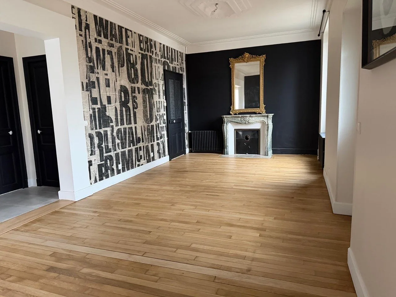 Pièce vide avec parquet en bois clair, papier peint typographique et cheminée en marbre