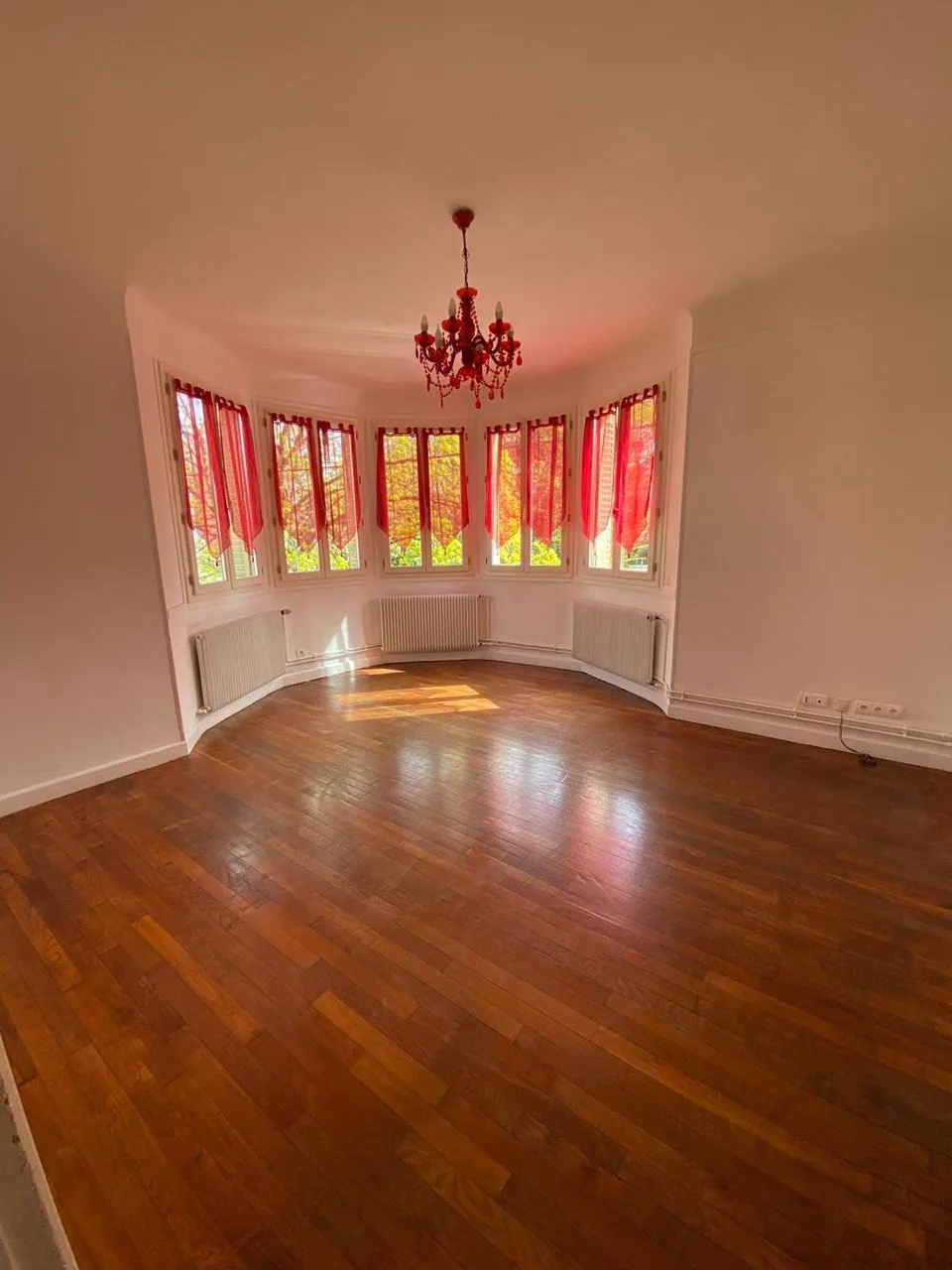 Pièce vide avec un parquet en bois ciré et une baie vitrée, lumière rasante sur le sol
