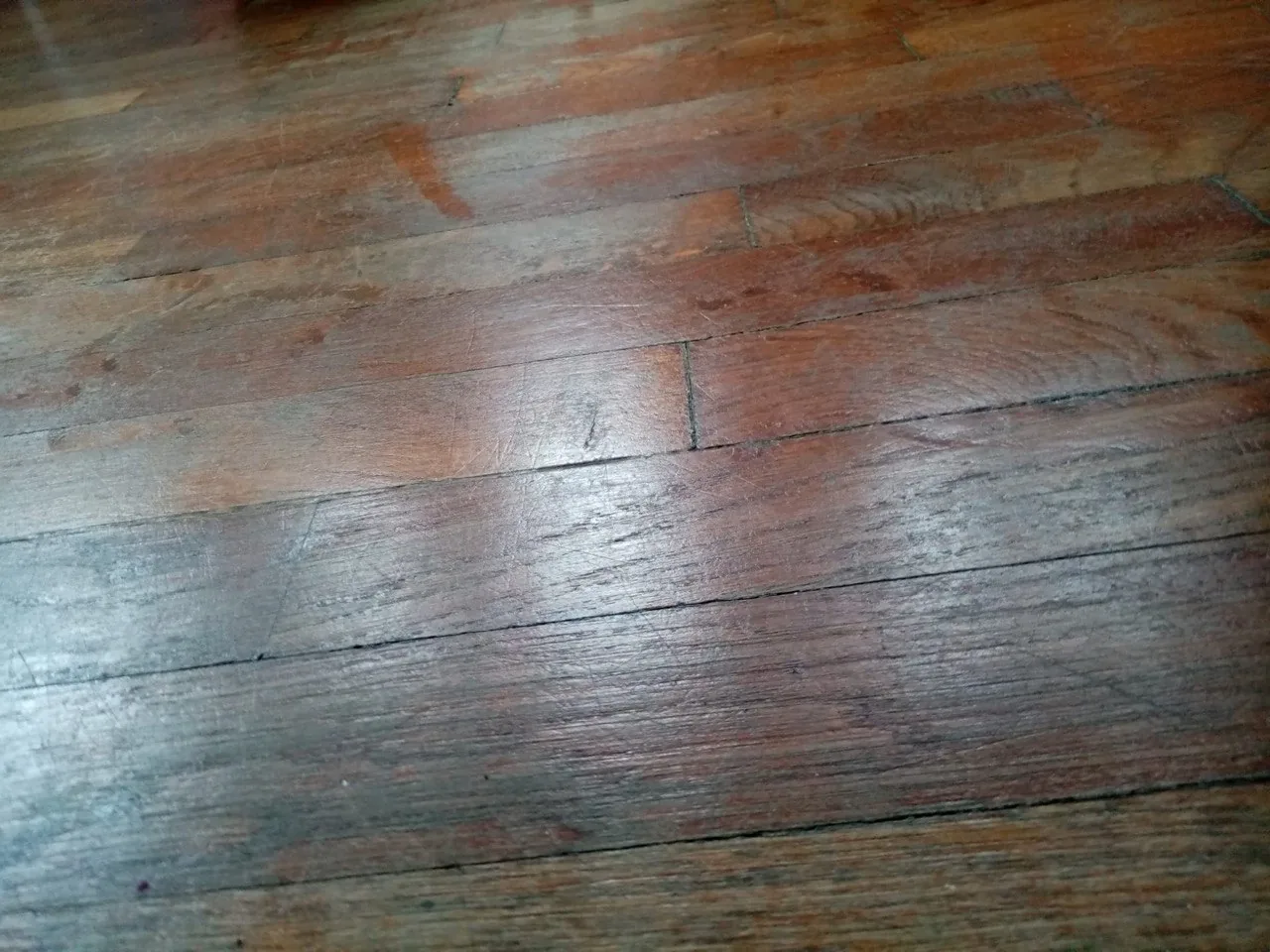 Lames étroites d'un parquet en bois usé, rayures et veinage visibles sous la lumière